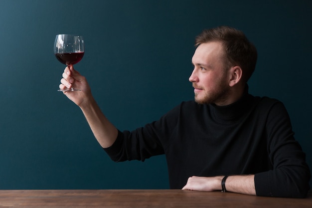 Degustazione di vini rossi. Brindisi maschile. Pubblicità di bevande alcoliche, giovane interessato al bar su sfondo blu con spazio libero. Bevanda squisita, celebrazione della festa, concetto di gusto