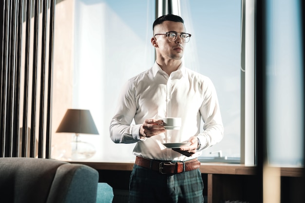 Del caffè. Elegante giovane uomo d'affari ricco che indossa camicia quadrata scura bere un caffè