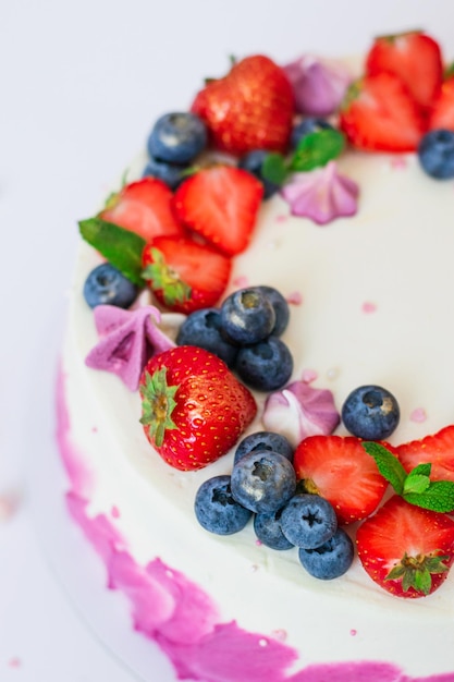 Delicata torta guarnita con fragole fresche mirtilli su sfondo rosa chiaro Dessert festivo con frutti di bosco