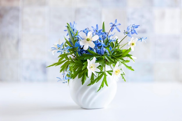 Delicato bouquet dei primi fiori primaverili anemone e bucaneve in un vaso bianco