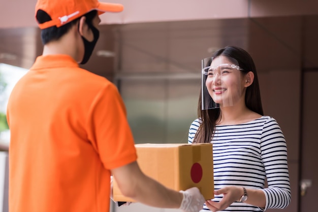 Deliveryman consegna a una donna di ufficio sorridente con scudo per il viso e maschera