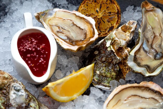 Delizia del mare ostriche aperte fresche disposte su ghiaccio su uno sfondo scuro lo sfondo è decorato con rami di eucalipto ostriche chiuse al limone e salsa