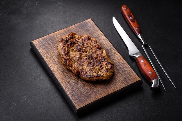 Deliziosa bistecca di maiale alla griglia succosa con spezie ed erbe aromatiche su un tagliere di legno