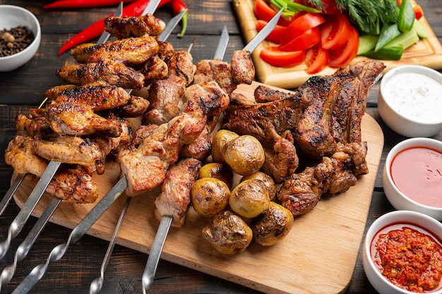 Deliziosa carne alla griglia assortita su spiedini con verdure fresche e patate al forno
