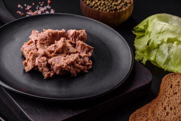 Deliziosa carne di tonno in scatola su un piatto di ceramica nera su uno sfondo di cemento scuro