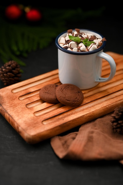 Deliziosa cioccolata calda con marshmallow e biscotti sul vassoio di legno sul primo piano nero del fondo