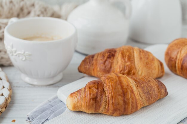 Deliziosa colazione con croissant freschi e tazza di caffè su un bianco di legno