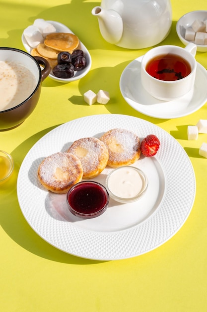 Deliziosa colazione con formaggio cottage pancake farina d'avena tè miele marmellata frutta su tavola gialla