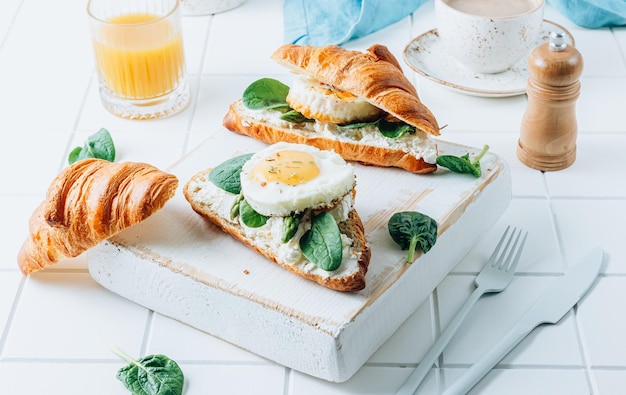 Deliziosa colazione con panini croissant con spinaci all'uovo fritto e caffè e succo d'arancia