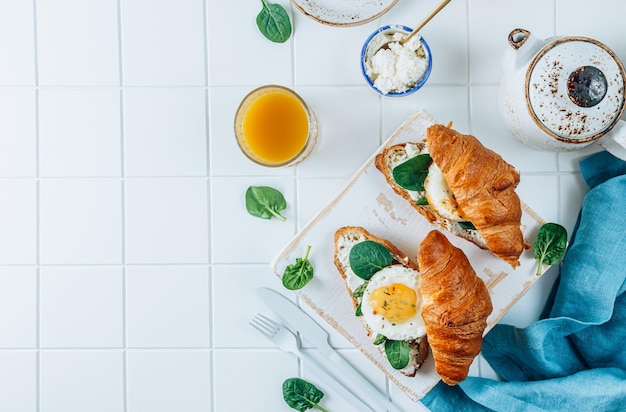 Deliziosa colazione con panini croissant con spinaci all'uovo fritto e caffè e succo d'arancia