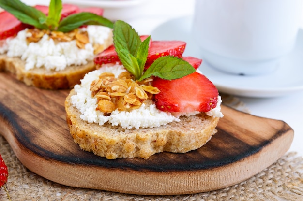 Deliziosa colazione dietetica sana: pane di segale con ricotta e fragole su un bianco di legno.