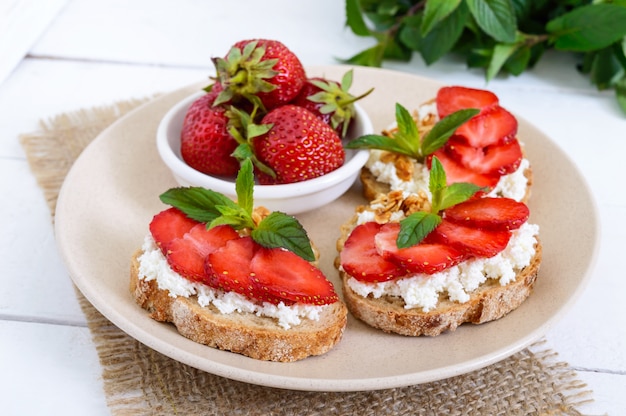 Deliziosa colazione dietetica sana: pane di segale con ricotta e fragole su un bianco di legno.