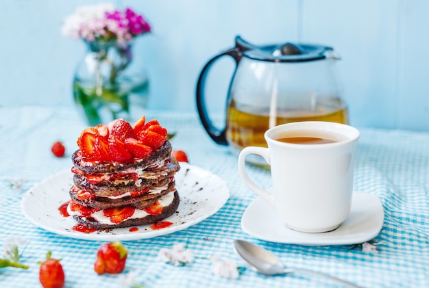 Deliziosa colazione nel deserto. Pila di pancake con marmellata e tè di frutta e fragola, in piatto bianco su una tavola blu.