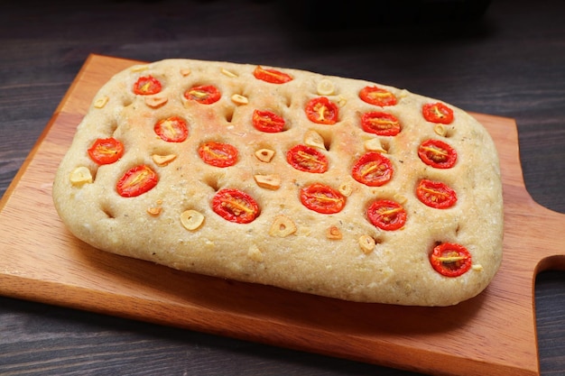 Deliziosa focaccia italiana appena sfornata con pomodoro e aglio su tagliere di legno