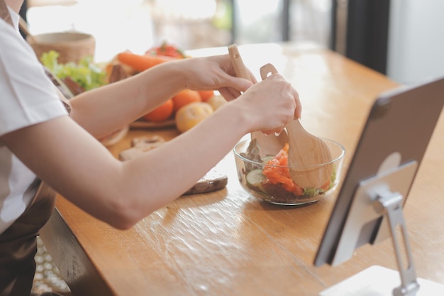 Deliziosa frutta e verdura su un tavolo e una donna che cucina La casalinga taglia i cetrioli verdi su una tavola di legno per preparare un'insalata fresca in cucina