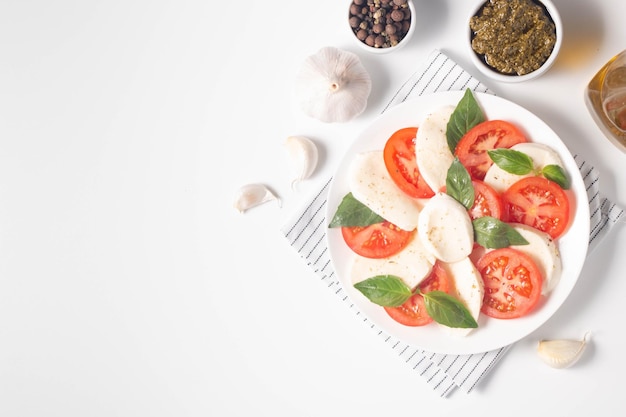 Deliziosa insalata caprese italiana con mozzarella a fette, pesto di basilico e aglio sullo sfondo