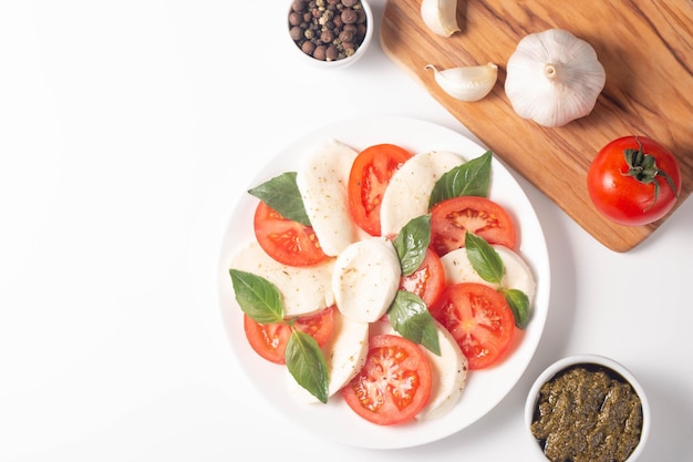 Deliziosa insalata caprese italiana con mozzarella a fette, pesto di basilico e aglio sullo sfondo