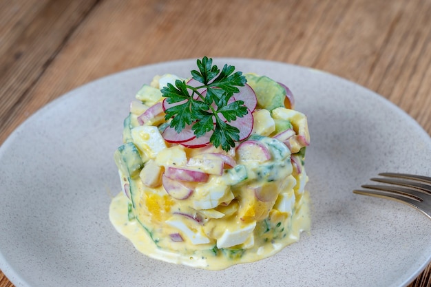 Deliziosa insalata con cetriolo, ravanello e uova sode con salsa di panna in un piatto su fondo di legno. Cibo sano, da vicino