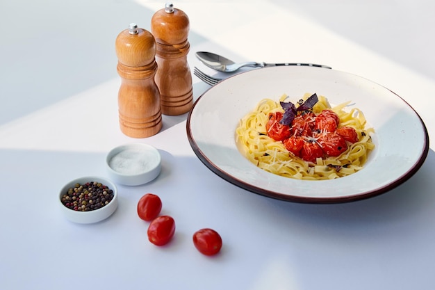 Deliziosa pasta con pomodori servita con posate sale e macinapepe sul tavolo bianco alla luce del sole