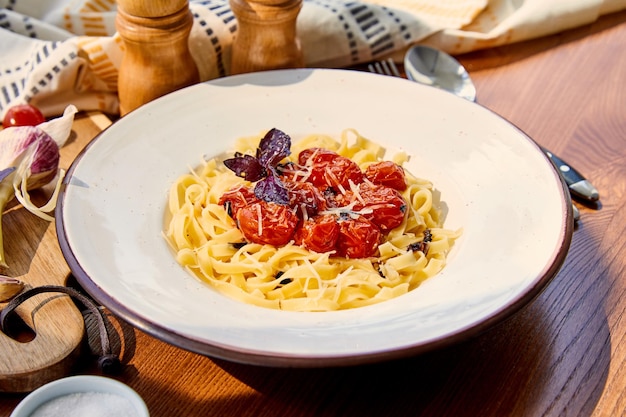 Deliziosa pasta con pomodorini parmigiano e basilico rosso servita su tavola di legno alla luce del sole