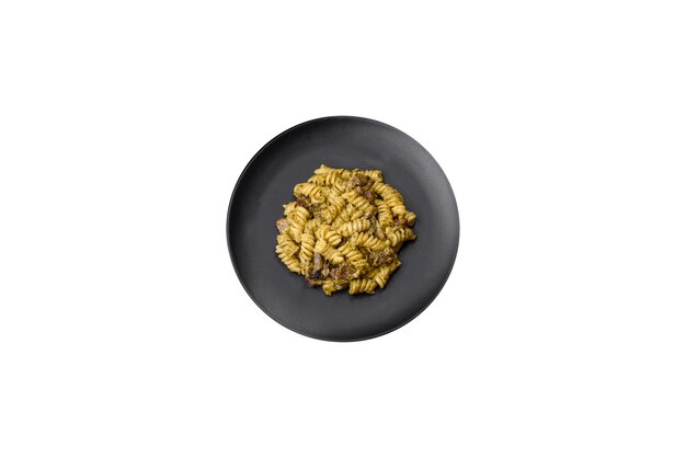 Deliziosa pasta fusilli con pesto verde con sale e spezie su un piatto di ceramica su uno sfondo di cemento scuro