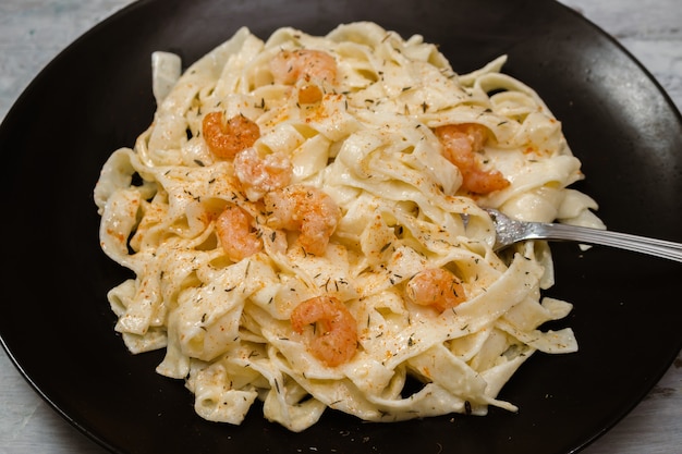 Deliziosa pasta italiana. Fetuccini con gamberi e salsa alle erbe su banda nera e sfondo chiaro.