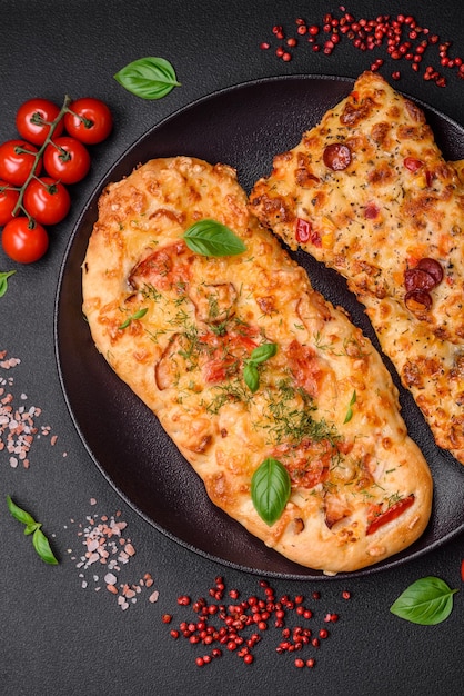 Deliziosa pizza focaccia fresca al forno con formaggio, pomodori, salsiccia, sale e spezie su uno sfondo di cemento scuro