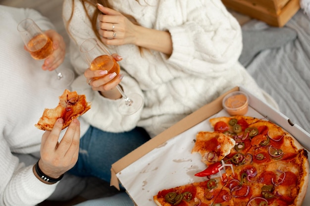 Deliziosa pizza fragrante e vino in bicchieri di vetro danno piacere a coppie innamorate in un appuntamento romantico...