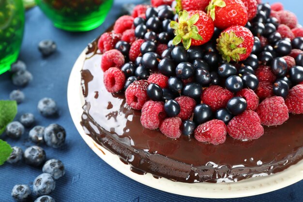 Deliziosa torta al cioccolato con frutti di bosco estivi sulla tovaglia blu primo piano