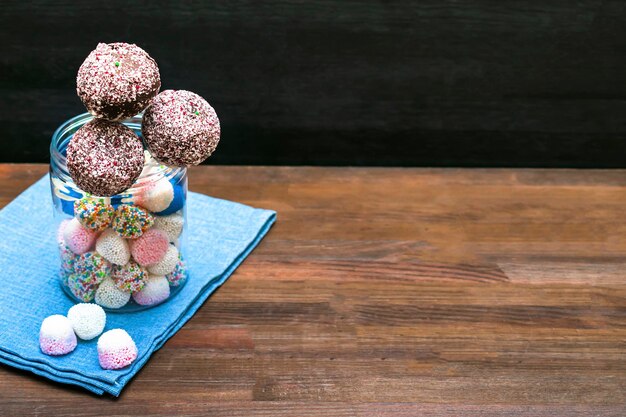 Deliziosa torta al cioccolato schiocchi decorati confettini bianchi in barattolo con caramelle colorate dolci sul tovagliolo sullo sfondo di legno dolci di pasticceria sul bastone con nastro adesivo Cibo gustoso