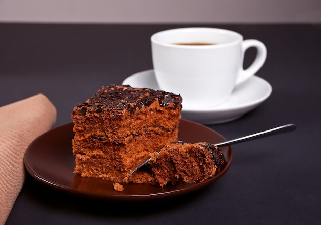 Deliziosa torta al cioccolato sul piatto marrone con una tazza di caffè sul tavolo nero