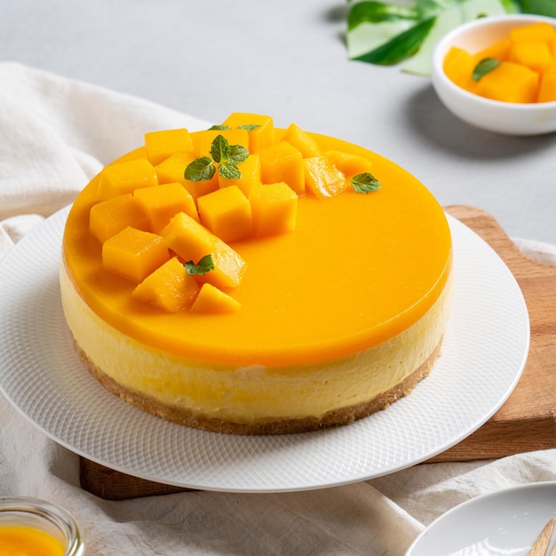 Deliziosa torta al mango glassata senza formaggio al forno con topping di polpa di mango fresca tagliata a dadini su sfondo luminoso del tavolo