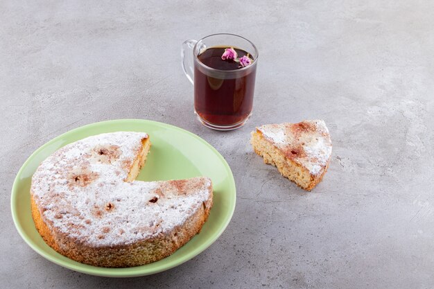 Deliziosa torta con zucchero in polvere e una tazza di tè in vetro.