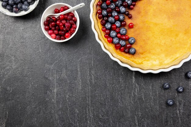 Deliziosa torta di cheesecake con mirtilli freschi e mirtilli rossi, su uno sfondo di pietra scura con spazio di copia.