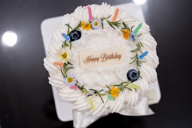 Deliziosa torta di cocco di compleanno decorata con bellissimi fiori e candela su sfondo grigio testurizzato