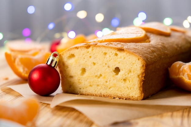 Deliziosa torta di mandarini con pezzi di mandarino, luci di Natale e giocattoli su fondo di legno. Ricetta facile della pasticceria fatta in casa, dolce vegano per le vacanze invernali. Buon Natale e Felice Anno nuovo.