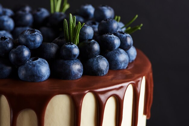 Deliziosa torta fatta in casa decorata con mirtilli freschi su un supporto in legno bianco