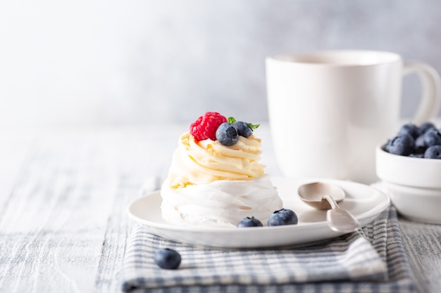 Deliziosa torta Pavlova con panna montata e frutti di bosco freschi. Tazza di caffè bianco.