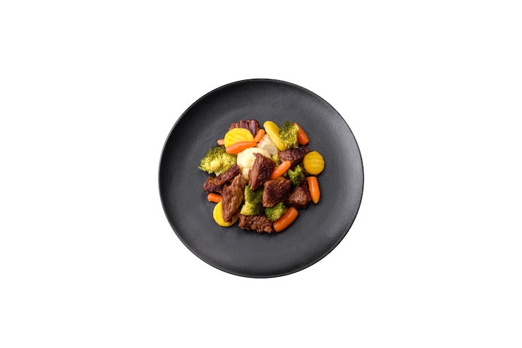 Foto deliziose carni fresche di manzo e verdure carote broccoli cavolfiore su un piatto nero su uno sfondo di cemento scuro