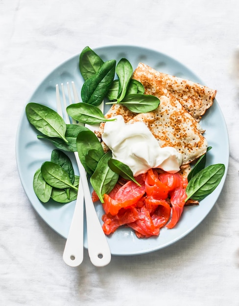 Deliziose crepes per il brunch della colazione con spinaci freschi di panna acida e salmone leggermente salato su uno sfondo chiaro vista dall'alto