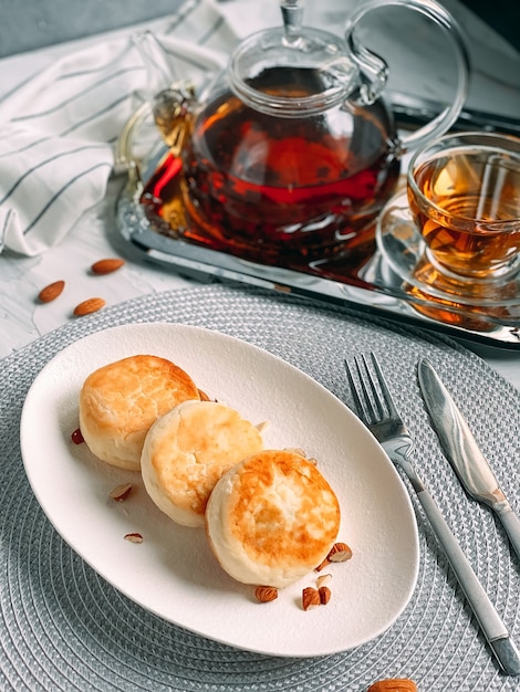 Deliziose frittelle di cheesecake con tazza da tè e teiera su vassoio d'argento su un panno da cucina