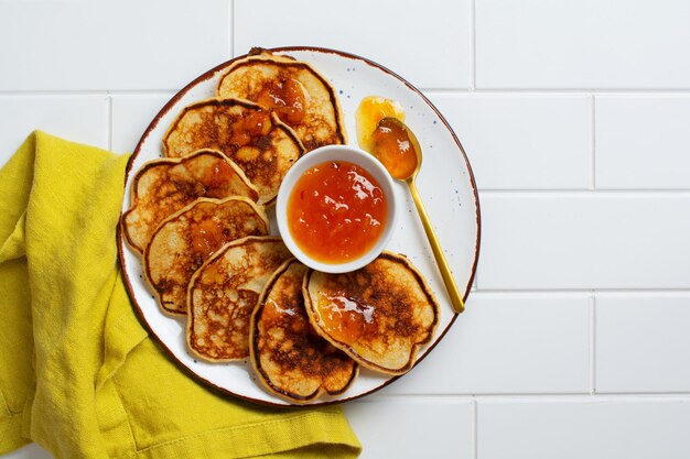 Deliziose frittelle fatte in casa con frutta fresca di albicocca e marmellata su uno sfondo chiaro di ardesia, pietra o cemento. Vista dall'alto con copia spazio