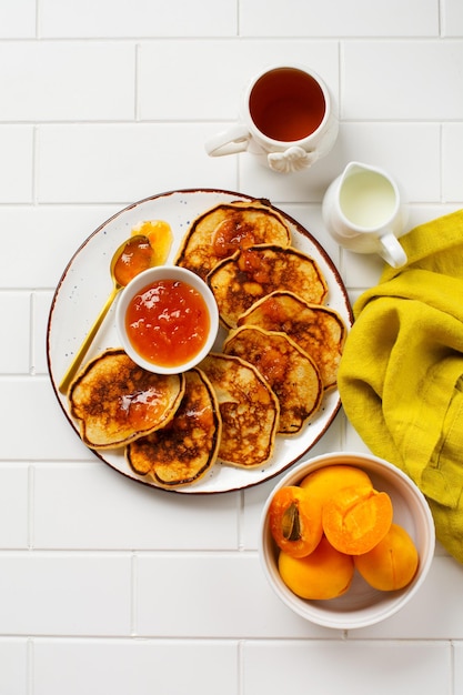 Deliziose frittelle fatte in casa con frutta fresca di albicocca e marmellata su uno sfondo chiaro di ardesia, pietra o cemento. Vista dall'alto con copia spazio