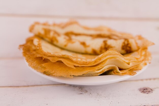 Deliziose frittelle rotonde sottili su un piatto bianco su un tavolo di legno in cucina