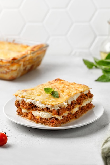 Deliziose lasagne con ragù di carne bolognese e formaggio su piatto bianco e sfondo grigio