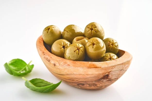 Deliziose olive verdi con foglie di rosmarino in una ciotola di legno, isolata su sfondo bianco.