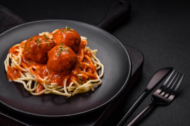 Deliziose polpette fresche e pasta in salsa di pomodoro con sale spezie ed erbe aromatiche su uno sfondo di cemento scuro