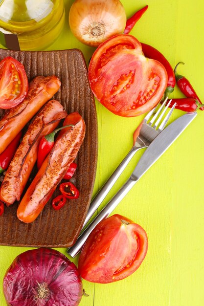 Deliziose salsicce con verdure sulla piastra sul primo piano della tavola di legno