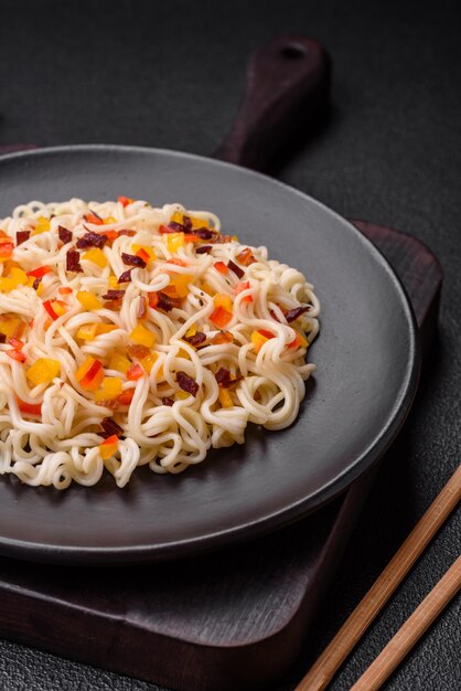 Deliziose tagliatelle asiatiche fresche con pezzi di carne di verdure con sale, spezie ed erbe su uno sfondo di cemento scuro