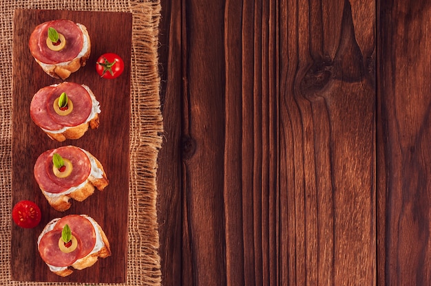 Deliziose tartine con salame con pomodorini su uno sfondo di legno - Vista dall'alto con spazio di copia